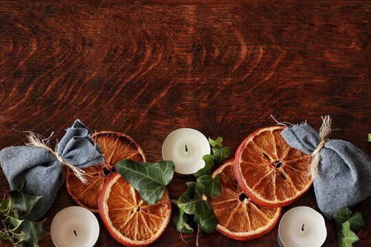 Dark brown wooden table background for text, decorated with dried orange, ivy evergreens, blue cotton bags to look festive and cozy for Yule winter solstice (Christmas). Free writing space at the top