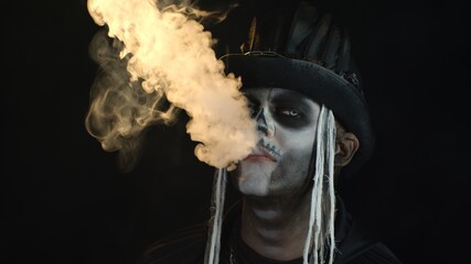 Frightening man in creepy skeleton Halloween cosplay exhaling cigarette smoke from his mouth