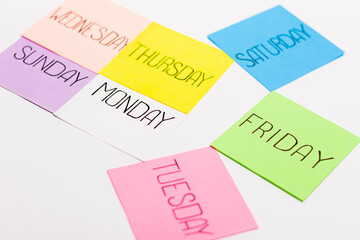Sheets of paper in different colors are arranged in the shape of an arrow. Piece of paper has the name of one day of the week written on it.