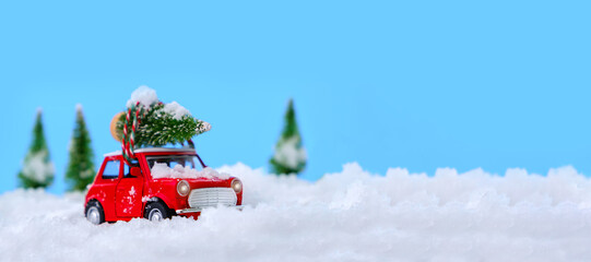Christmas tree on red car toy with blurred tree background and snow.