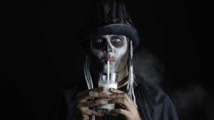 Creepy man with skeleton makeup in top-hat. Guy looking at camera, drinks milk from a glass