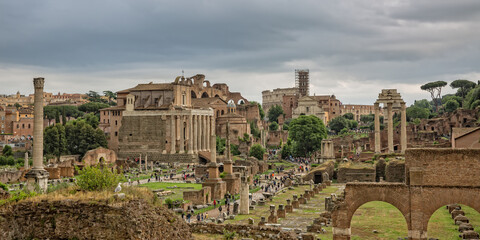 Fototapeta premium Panoramic view of the ruins the Roman Forum. Tourists visit the Roman Forum ancient ruins in the historic center of Rome, Italy