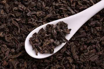 Dry tea leaves in a white porcelain spoon. Black tea leaves close up.