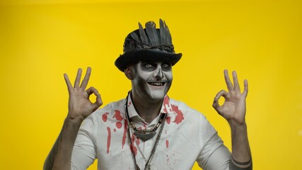 Sinister man with horrible Halloween skeleton makeupmaking faces, looking at camera, showing ok sign