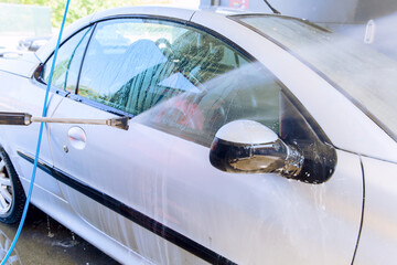 Washing car with pressure washer at self-service car wash station