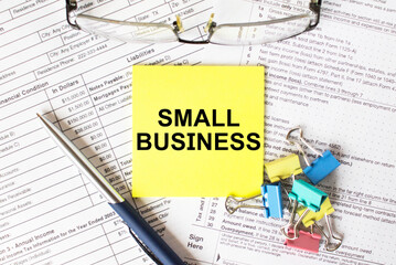 Yellow sticker with text Small Business. Next to it is a blue pen with colored stationery clips and eyeglasses