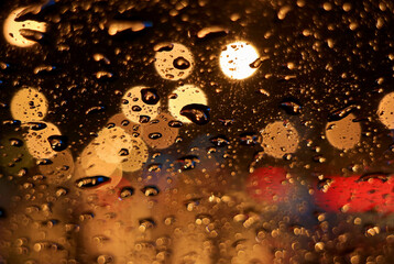 Closeup raindrops on the car windshield surface, with blurry urban street lights at night	