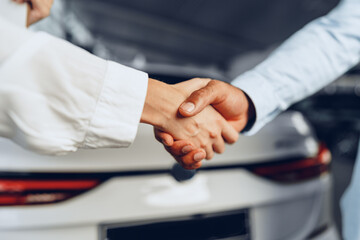 Car seller and buyer handshake at car dealership against a new car