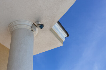 Surveillance cctv (closed circuit television) camera installed on roof of private house on blue sky background for protection against crime. Bottom view. Horizontal