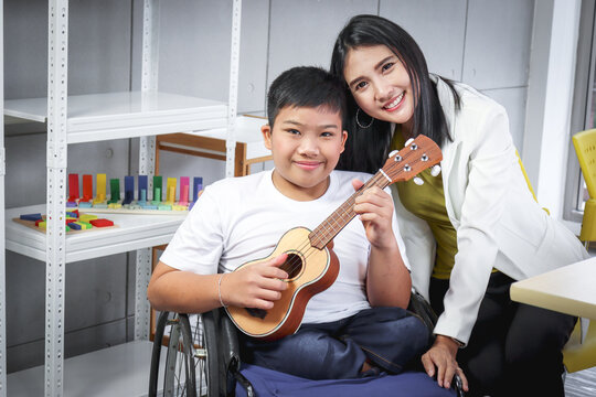 Disabled kids classroom, children having fun during study at school with teacher, kid learning and playing, schoolboy on wheelchair playing ukulele