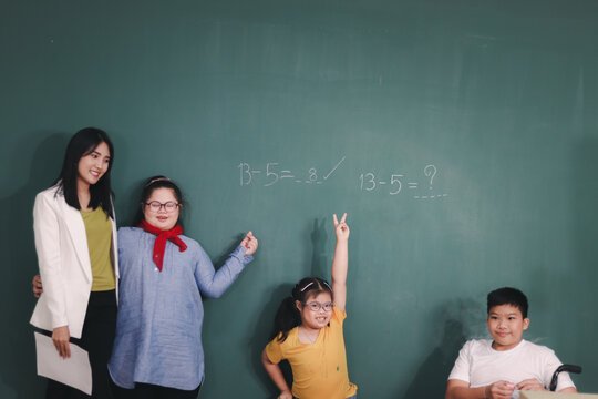 Disabled kids classroom, school boy on wheelchair and down syndrome girls learning and having fun during study at school with teacher, they writing on the blackboard