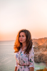 A young woman tourist stands on the shore high above the sea at sunset and admires Cape Fiolent in the Crimea