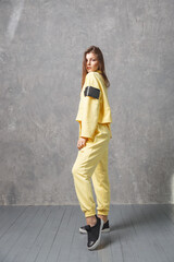 Young woman in yellow sportswear, pants and sweatshirt. Concept of fashionable sport outfit, indoors photo. Copy space.