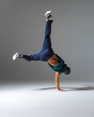Cool b-boy dances on the floor standing on one hand isolated on gray background. Breakdance lessons