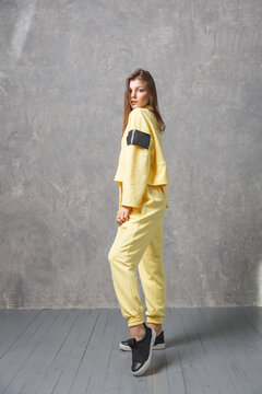 Young Woman In Yellow Sportswear, Pants And Sweatshirt. Concept Of Fashionable Sport Outfit, Indoors Photo. Copy Space.