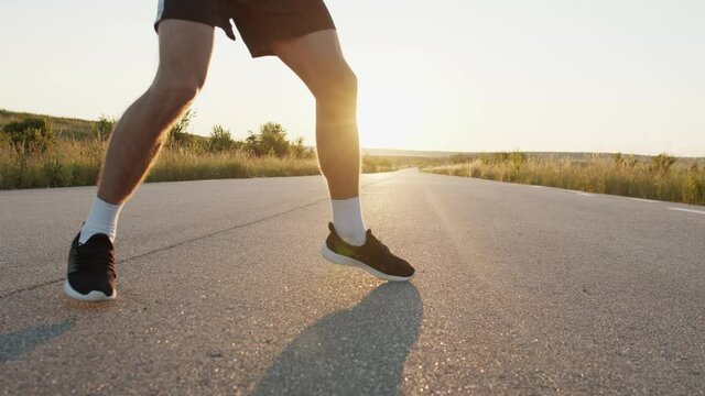 Low view of kickboxer training kicks on road singly during blinding sunset