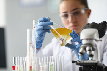 Woman chemist holds flask with yellow liquid in her hands in chemical laboratory. Quality control...