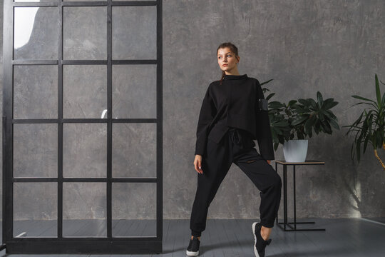 Young woman in black sportswear, pants and sweatshirt. Concept of fashionable sport outfit, indoors photo. Copy space.