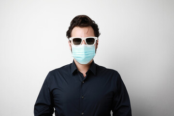 Portrait of young man in medical mask and sunglasses, stands on white background. Pandemic situation, Covid-19.