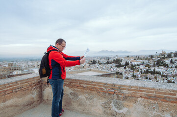 A man with a backpack is looking at a map over the background of a spanish small town