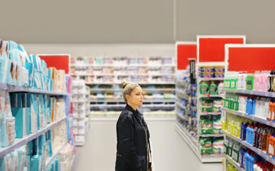 Woman shopping in supermarket reading product information.(shampoo, soap, shower gel,)	

