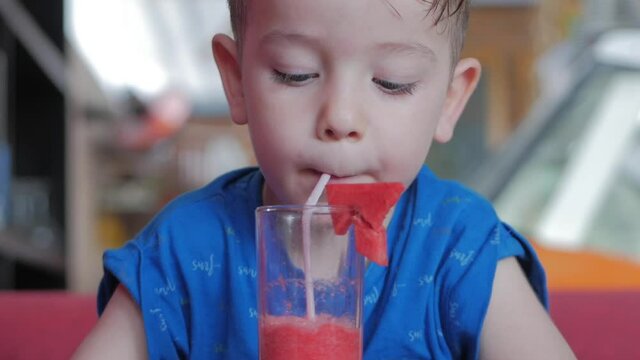 Cute baby boy drinking a glass of watermalon in a cafe. little boy drinking water. Close-up. The child is drinking a cup of juse.