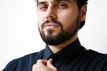 Close-up of handsome young man with beard in blue shirt looking with serious expression in camera.