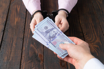 men's hands give money to women's hands in handcuffs against the background of a wooden table
