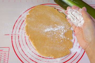 Hand sprinkling flour on dough while rolling for the concept of amateur cook baking at home