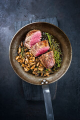 Fried dry aged beef fillet steak natural with king trumpet mushroom and herbs offered as top view in a rustic frying pan