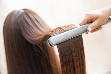 Close up hands of professional hairdresser beauty salon, straighteners curling female hair