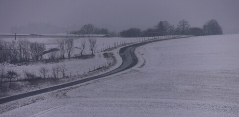 Panoramic view of a snow covered Eifel mountains winter landscape scenery with farm buildings and a curvy country road in Germany
