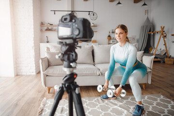 Fototapeta na wymiar Fitness woman blogger recording video on camera, training home in living room. Concept Lifestyle influencer sport and recreation