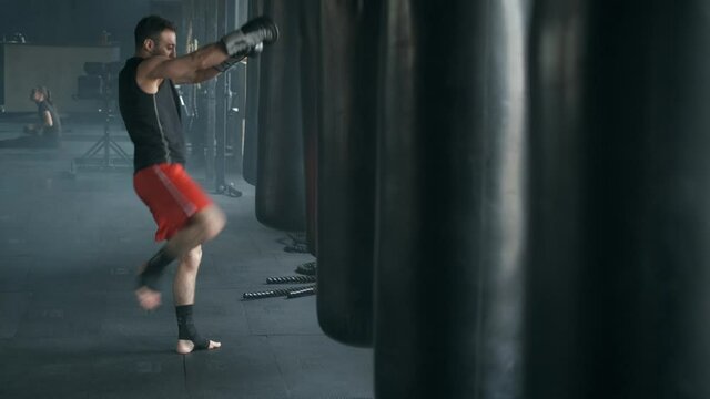 Aggressive professional fighter is training with a punching bag, inflicting a furious blow. The champion is engaged in kickboxing in the sports club. 4K 50fps footage