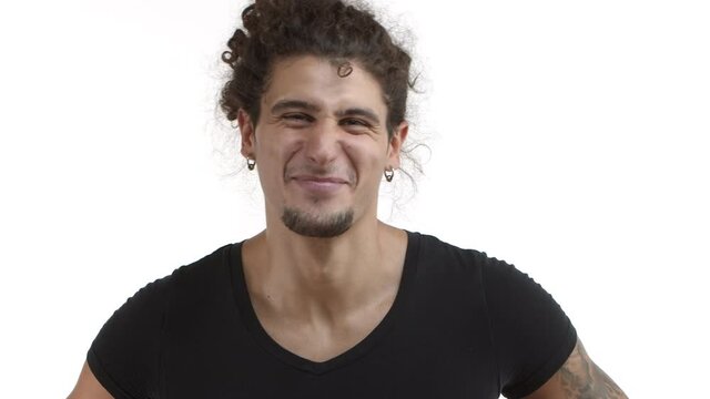 Close-up of attractive hispanic man with curly ponytail and beard looking happy, nodding in approval and smiling, laughing while standing in black casual t-shirt over white background
