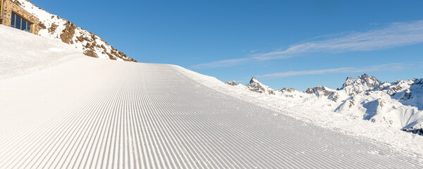 Close-up straight line rows of freshly prepared groomed ski slope piste with bright shining sun and...