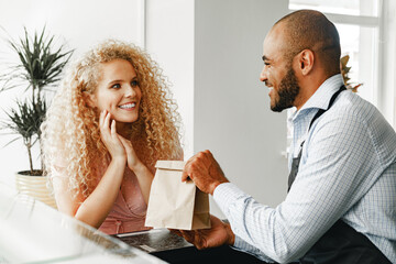 Smiling blonde woman talking to a waiter of a coffee shop at the counter