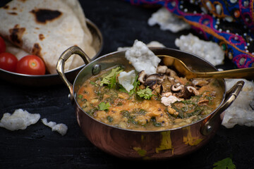 Indian spinach and lentil stew, saag dal, with flat breads on dark table