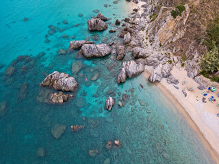 Aerial view of a beach and umbrellas. Tropea, Calabria, Italy.  Parghelia. Overview of seabed seen from above, transparent water. Swimmers, bathers floating on the water. Beach and rocks of Vardanello