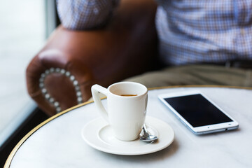 Businessman sitting in cafe, drinking morning coffee and using smartphone