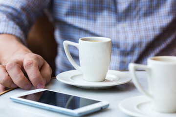 Businessman sitting in cafe, drinking morning coffee and using smartphone