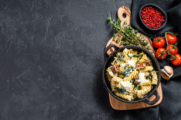 Delicious pasta fusilli dish with creamy spinach sauce and dried tomatoes.  Black background. Top view. Copy space