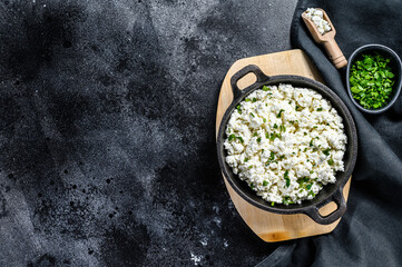 Cottage cheese in a cast-iron bowl with herbs. Organic dairy products. Black background. Top view. Copy space