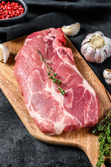 Raw pork cutlet steak. Piece of raw meat ready for preparation with greens and spices.  Black background. Top view