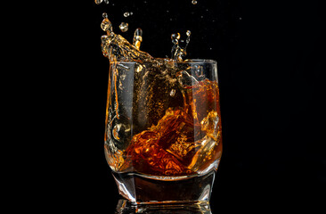 a glass of whiskey with ice from the spray on black with reflection