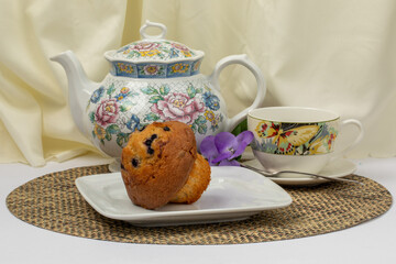 a blueberry muffin on a plate with a colorful teapot