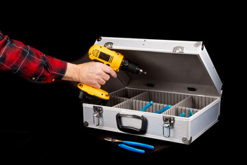 a worker in a red plaid shirt places an electric drill into an aluminum case isolated on black