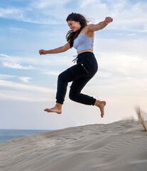 Fototapeta premium A smiling girl runs and jumps on the dunes of a beach.