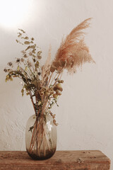 Glass vase with dry plants on the white wall. Minimalistic home decoration