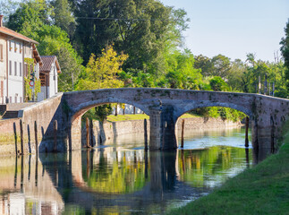 Fototapeta na wymiar ancient stone bridge reflected in the water of the navigable canal in the Ticino park near Milan on a sunny day.